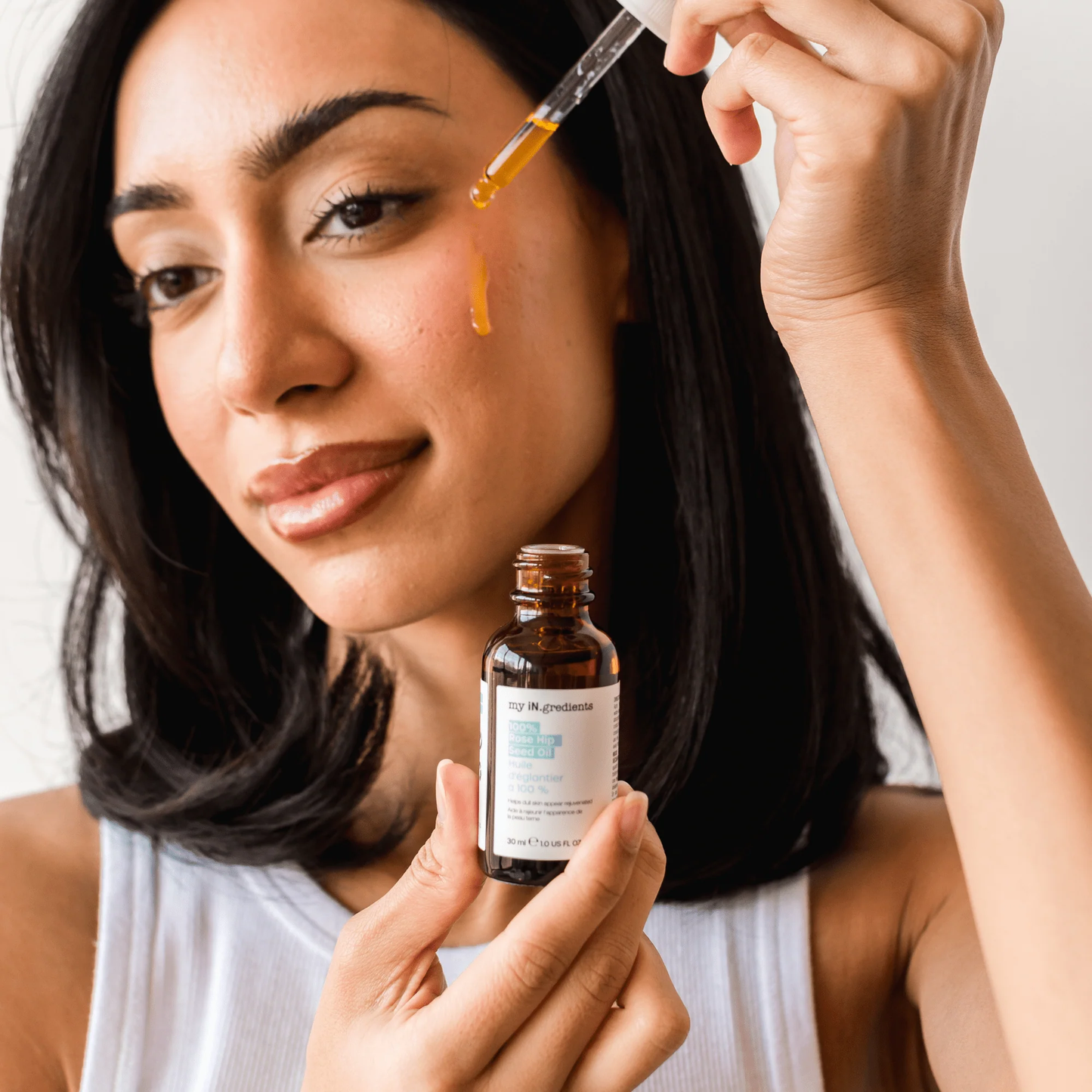 Amber glass bottle of my iN.gredients 100% Rose Hip Seed Oil 30ml with white dropper and minimal turquoise label, shown against a soft blue background, highlighting its pure, vegan formula for hydrating and soothing dull, dry, itchy facial skin.