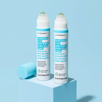 Slim turquoise tube of Masque BAR my iN.gredients Hyaluronic Acid Jade Stone Under-Eye Roller with jade tip exposed on a blue background, a cooling vegan treatment that hydrates, brightens dark circles and softens fine lines under the eyes.
