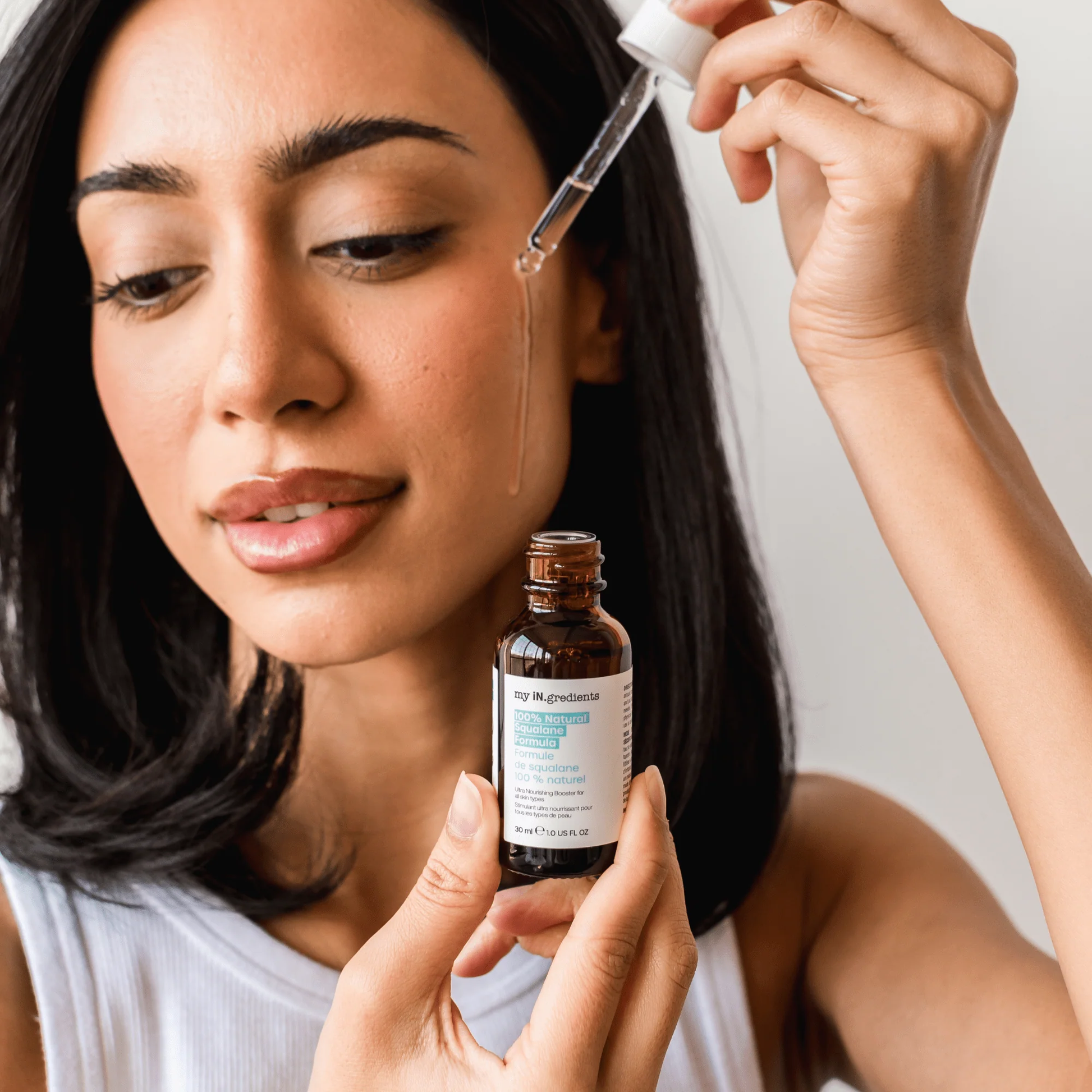 Amber glass bottle of my iN.gredients 100% Natural Squalane Formula 30ml with white dropper and turquoise label on rippling water background, highlighting a lightweight vegan oil that seals in moisture and soothes dry, red skin.